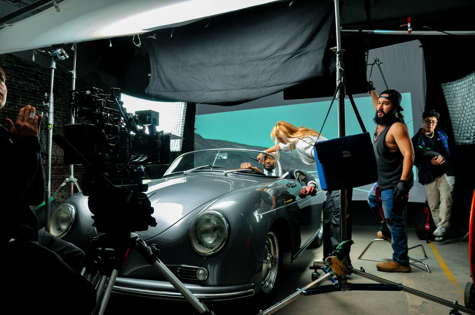 A film crew, cinema camera and lighting equipment around a convertible on a studio set.