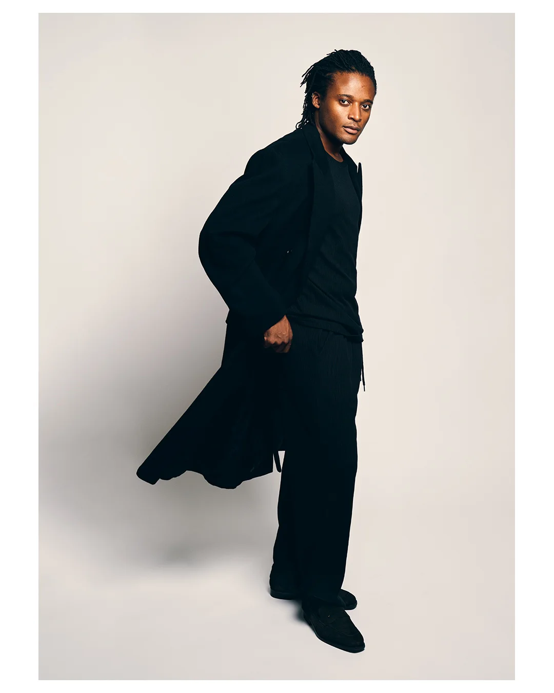 Full-length colour portrait of Kudzai King in a black coat.