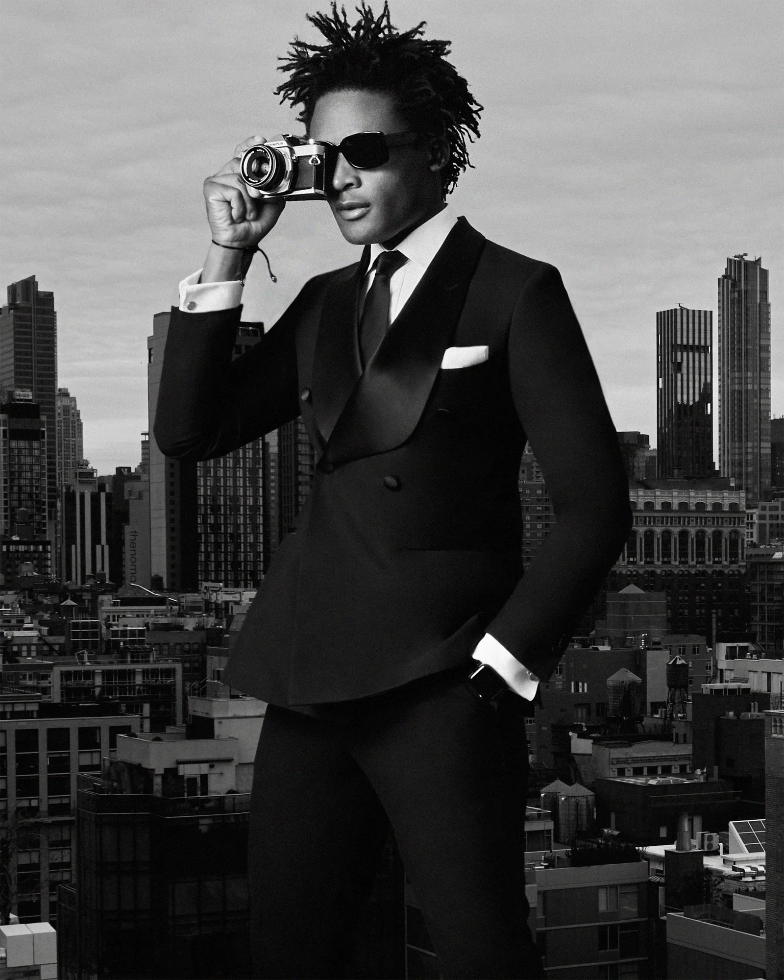 Black-and-white rooftop portrait of Kudzai King in a suit and sunglasses.
