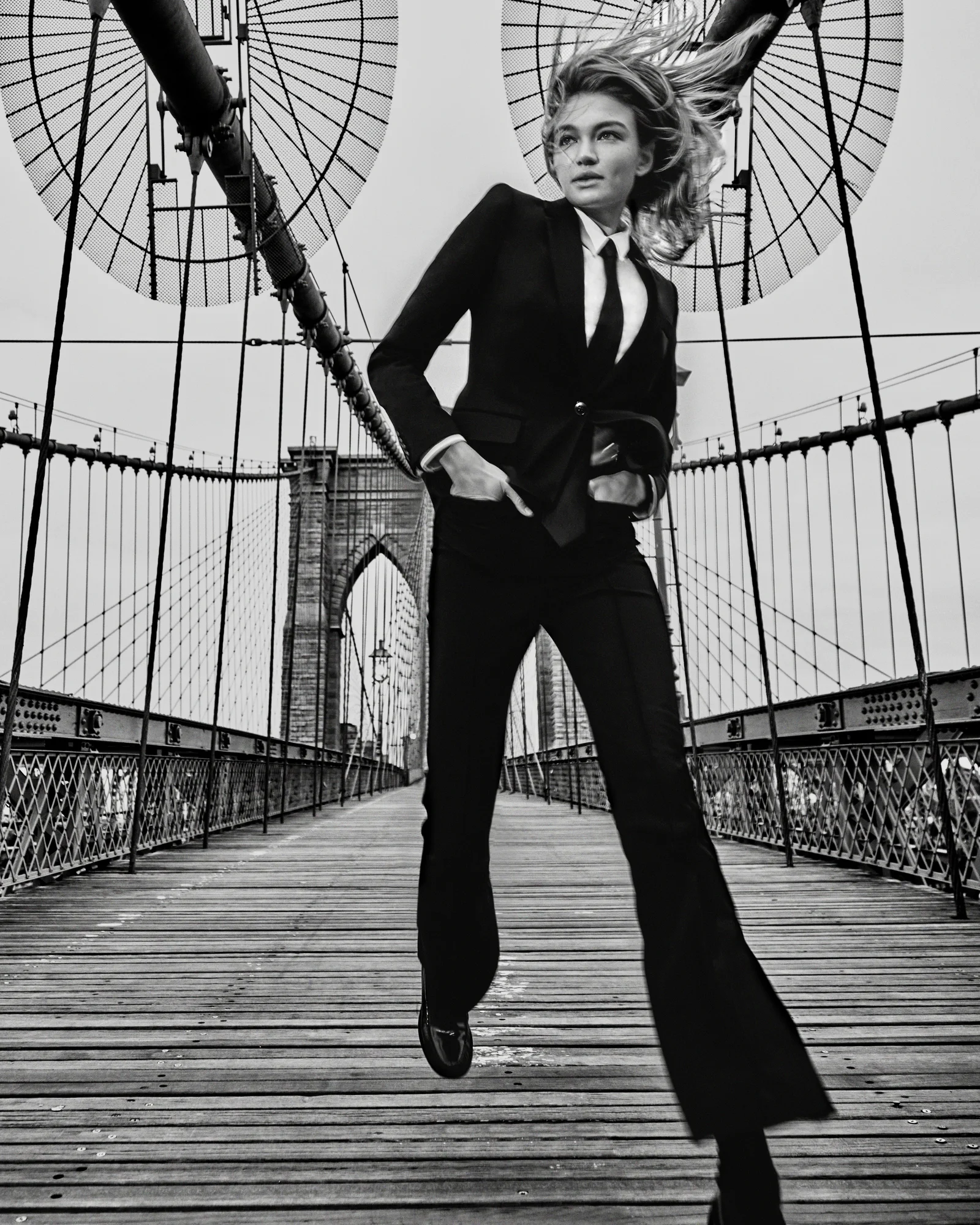 A model moving across the Brooklyn Bridge in black tailoring.