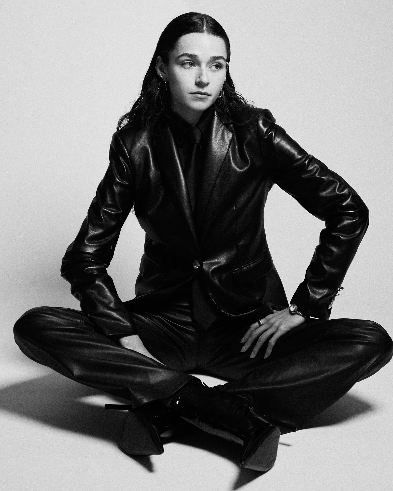 Black-and-white portrait of a model sitting cross-legged in black leather.
