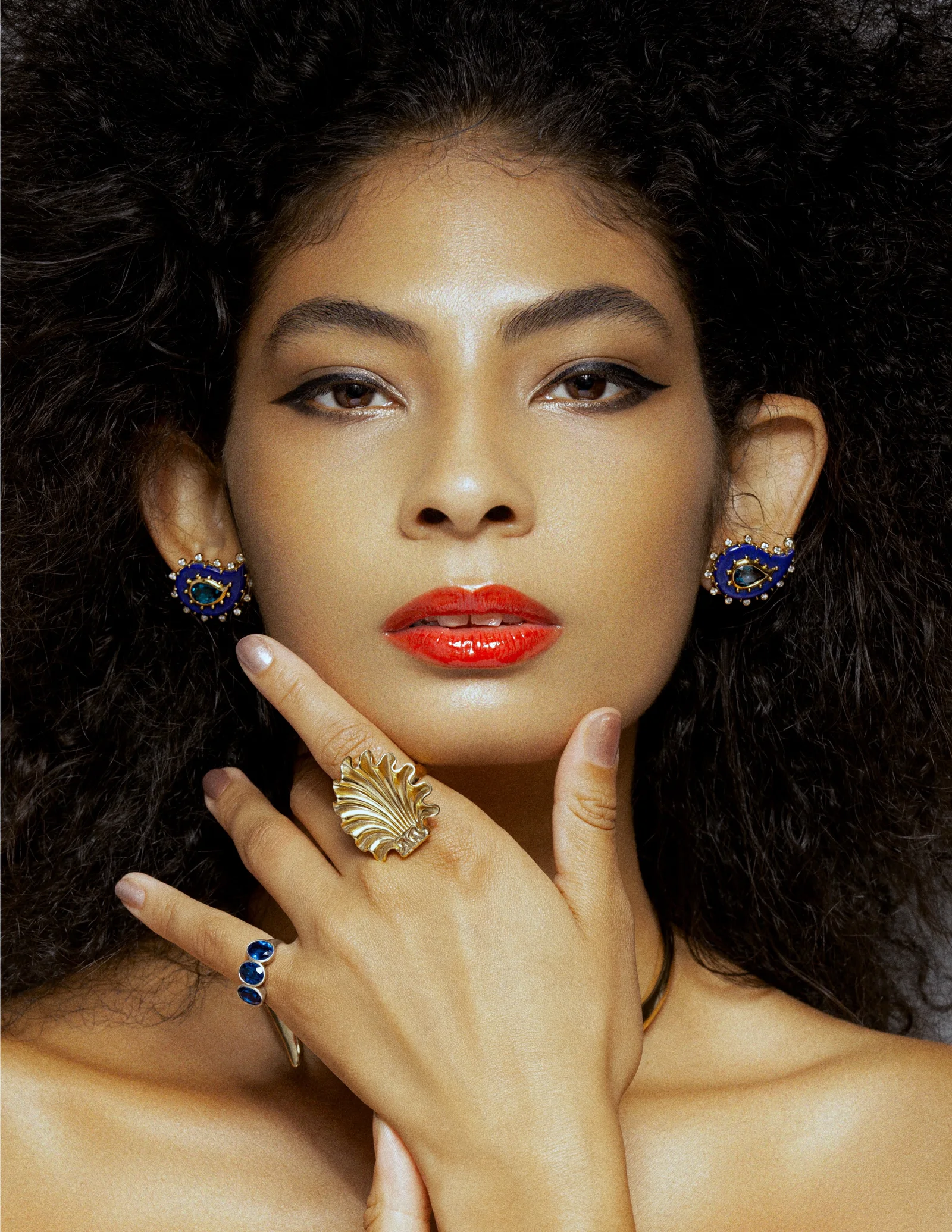 A close beauty portrait with red lips, coloured earrings and rings.