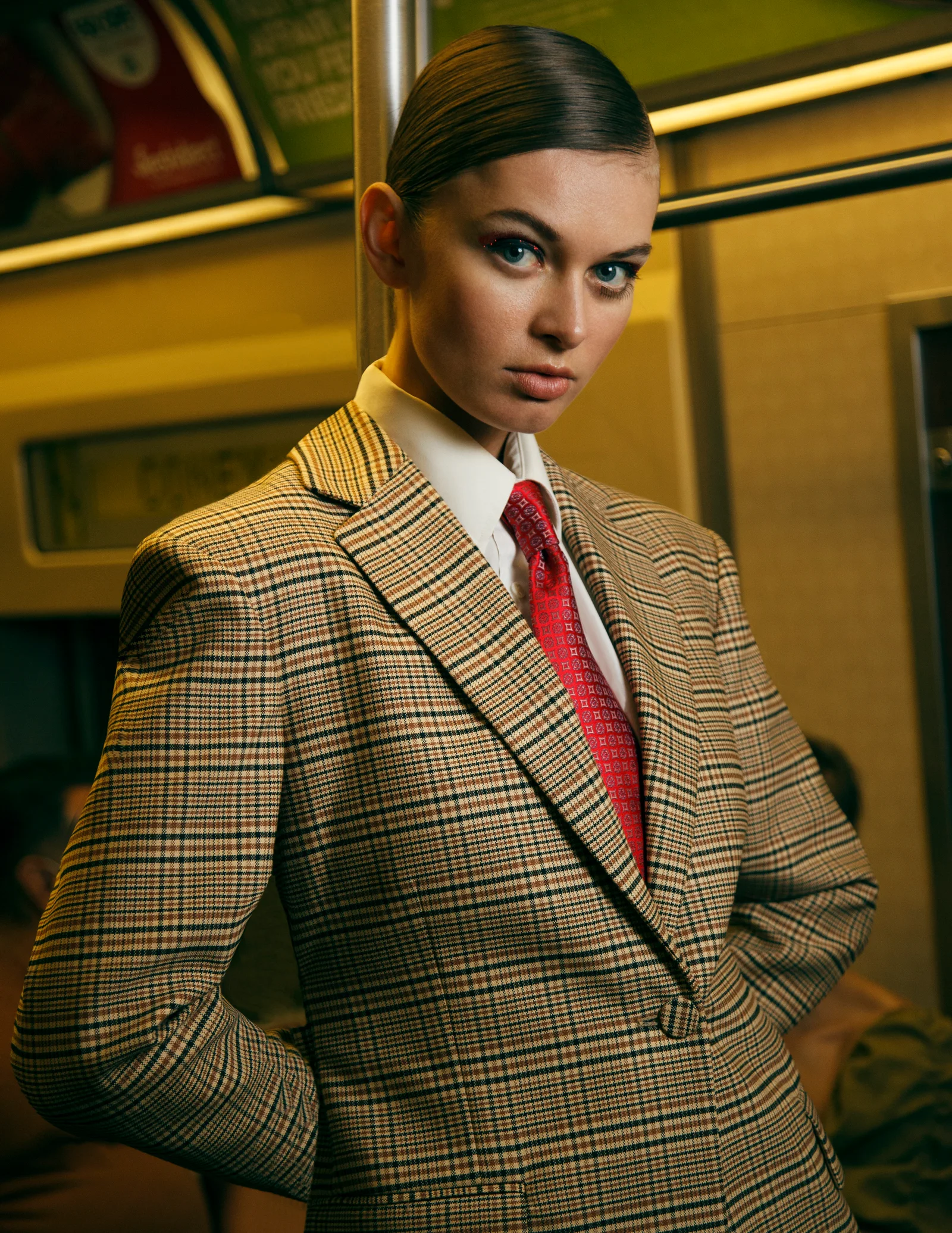 A close portrait in checked tailoring and a red tie on a subway platform.