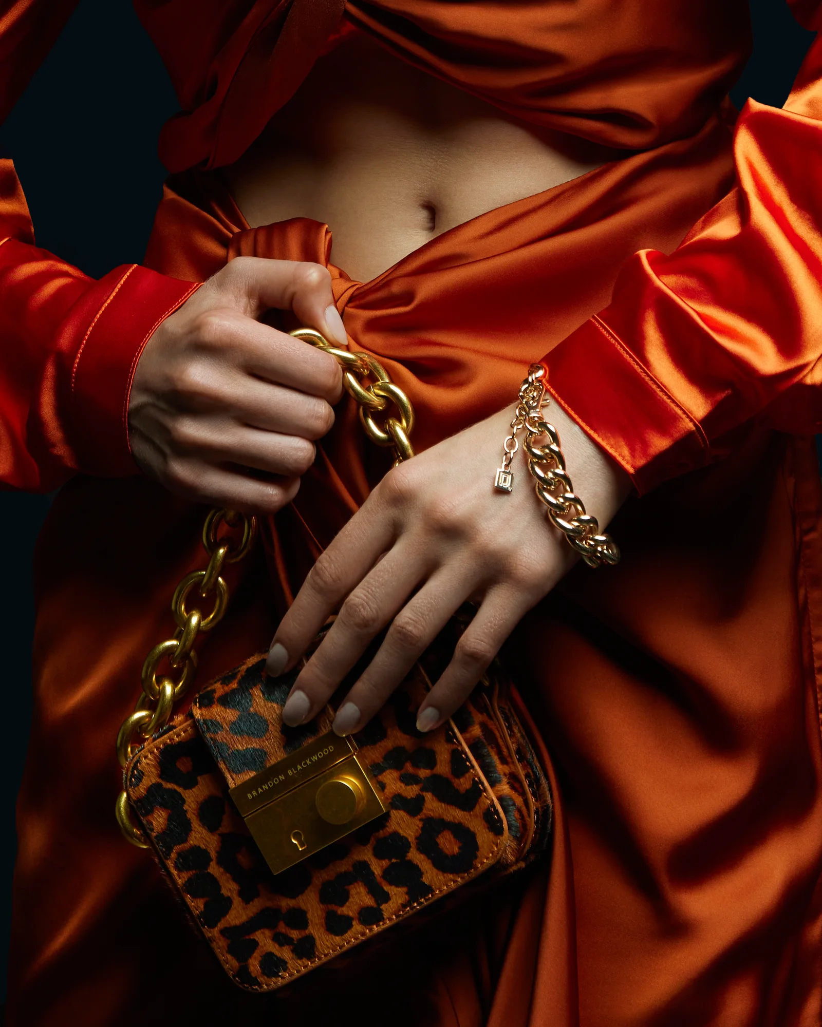 Hands, gold jewellery and a patterned handbag against orange satin.