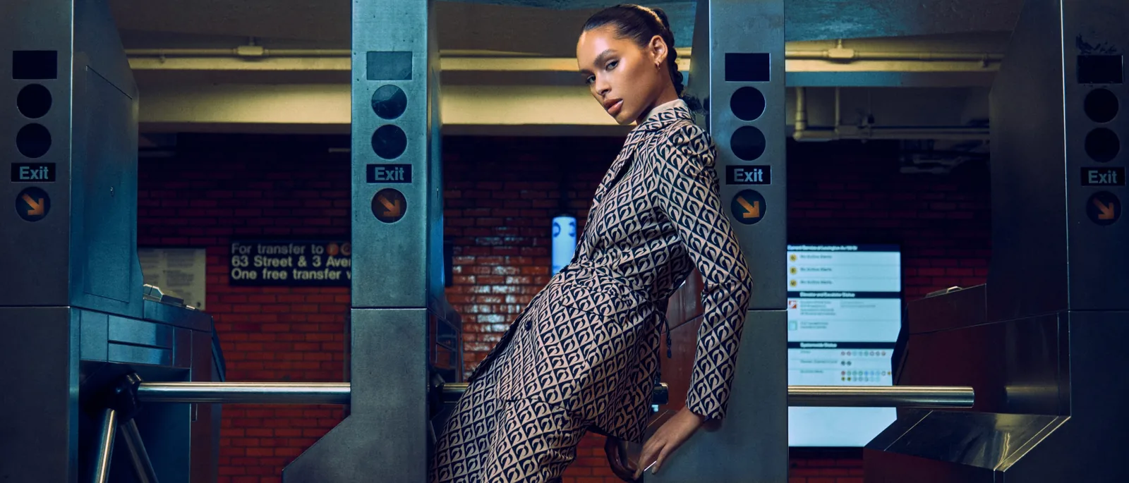 A model in patterned tailoring beside New York subway turnstiles.